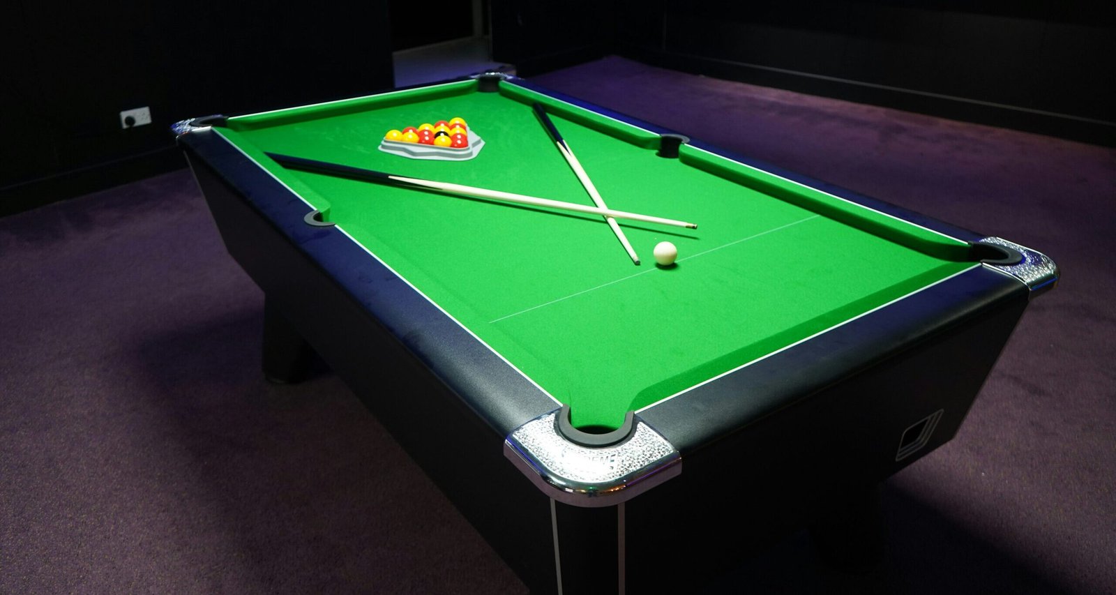 Green billiards table with a triangle rack of colorful balls, white cue ball, and two pool cues