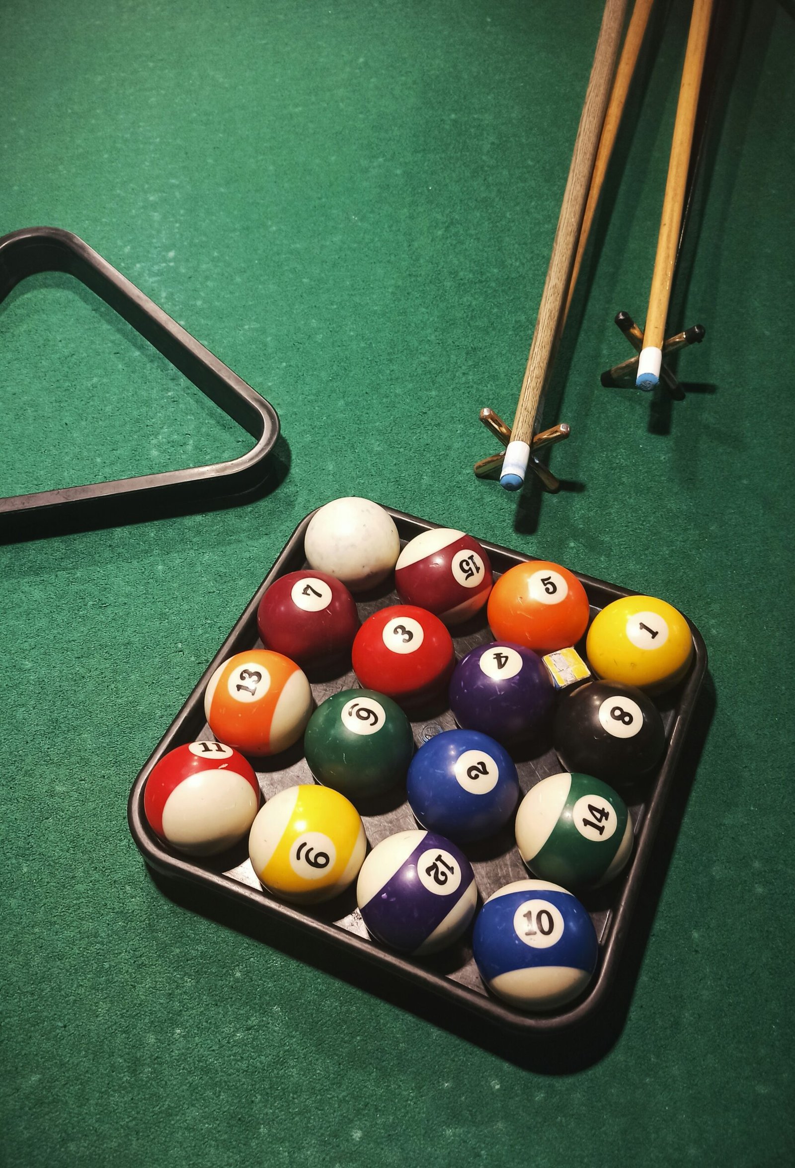 Close-up of billiard balls in a triangle rack on a green pool table with two pool cues